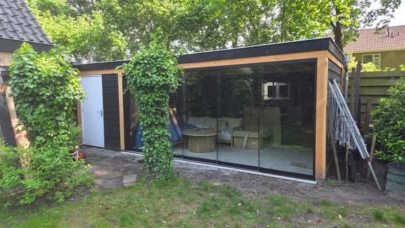 Dezelfde tuinkamer van voren, met de glazen schuifpui dicht en klimop tegen de staanders